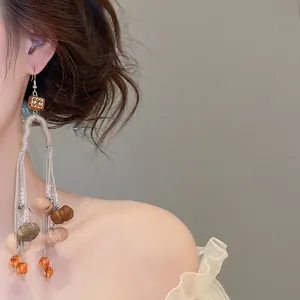 Close-up of vintage autumn pumpkin tassel earrings worn with elegant white dress