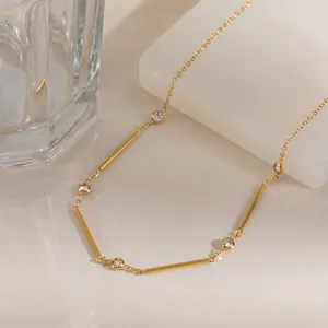 Detail view of a gold geometric necklace with zirconia and bar charms on a warm background