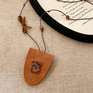 Detailaufnahme eines Bärenanhängers aus Harz an einem braunen Wildleder-Halsband.