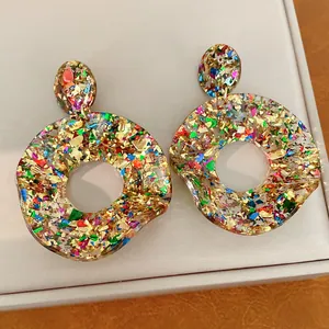 Nahaufnahme von bunten Glitzer-Acryl-Ohrringen in runder, hohler Form mit Silberstiften