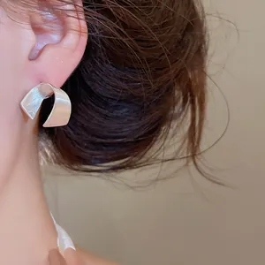 Primo piano dettagliato di orecchini a lobo minimalisti a forma di C in argento spazzolato.