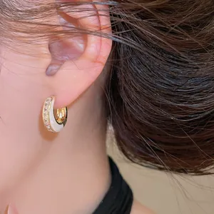 Nahaufnahme eleganter goldfarbener geometrischer Creolen mit weißem Emaille und klaren Kristallen