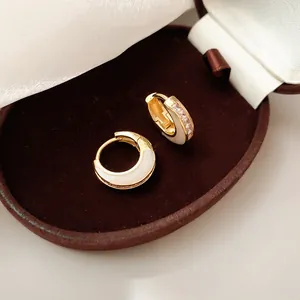 Nahaufnahme eleganter zweifarbiger geometrischer Creolen in Gold und Weiß mit Kristallen