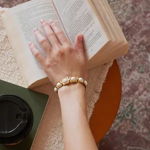 Détail d'un bracelet en acier inoxydable doré avec des perles de verre blanches au poignet