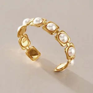 Gros plan d'un bracelet jonc ouvert en acier inoxydable doré avec d'élégantes perles blanches.