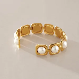 Détail d'un bracelet jonc en acier doré serti de perles de verre blanches carrées