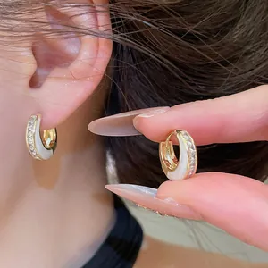 Detailaufnahme der geometrischen Goldohrringe mit weißer Einlage und Kristallen