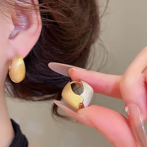 Nahaufnahme von gebürsteten zweifarbigen geometrischen Creolen in Gold und Silber.