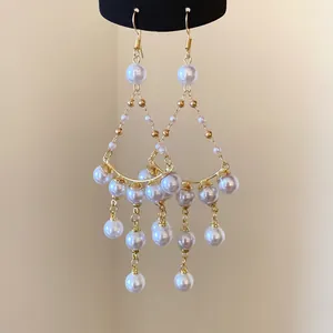 Close-up detail of elegant gold tassel earrings with white pearls and hooks.