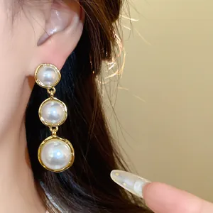 Close-up view of French style tiered pearl drop earrings with elegant textured gold frames.
