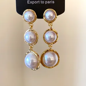 Detailed macro shot of French-style gold-tone triple drop pearl earrings.