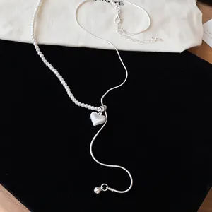 Gedetailleerde weergave van een asymmetrische zilveren ketting met parels en hart.
