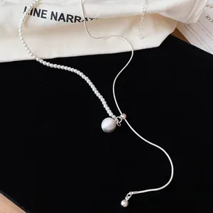 Gedetailleerde weergave van een asymmetrische zilveren ketting met witte parels en kraal