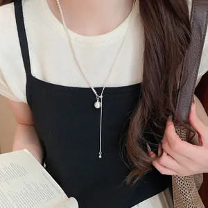 Detail van elegante asymmetrische zilveren ketting met kraalhanger gedragen door model.