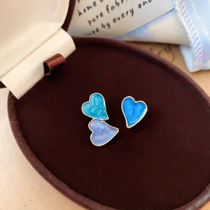Asymmetrical blue heart enamel stud earrings in a luxury brown velvet jewelry box.