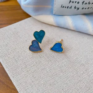 Close-up of asymmetric heart stud earrings featuring a vibrant blue enamel finish and gold edges