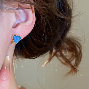 Macro view of a blue heart-shaped enamel stud earring with gold-toned metal trim