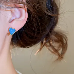 Detailed macro view of a vibrant blue enamel heart-shaped stud earring worn on a model