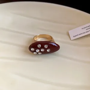 Close-up of retro burgundy enamel oval ring with sparkling inlaid crystals in gold finish