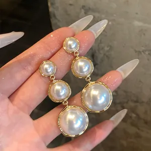 Detail view of French luxury drop earrings with graduated round white pearls in gold frames.