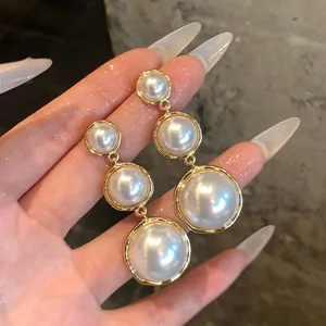 Detail view of French luxury drop earrings with graduated pearls and gold circular settings.
