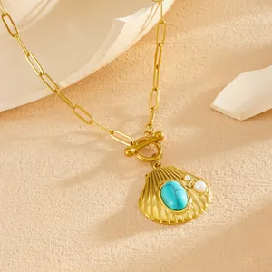 Detailopname van de gouden schelphanger met een turquoise steen en kleine parels