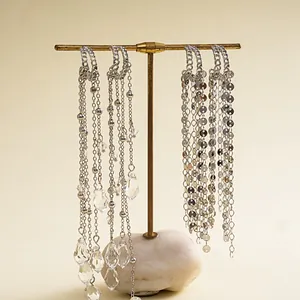 Detail of long silver tassel earrings with glass waterdrops and sequins on a display stand.