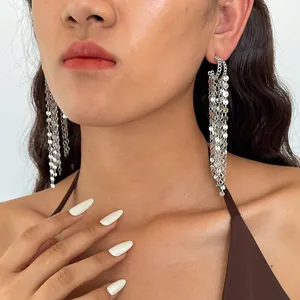Close-up view of long shimmering silver metal tassel earrings with sequin details on a model