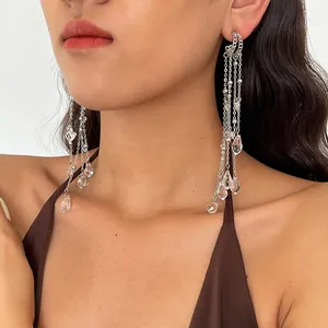 Close-up of silver tassel earrings with transparent glass water droplets worn by a model.