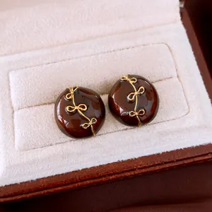 Nahaufnahme brauner runder Ohrstecker mit goldener Schleife und glänzendem Finish