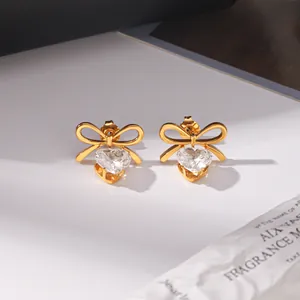 Close-up of 18k gold plated bow and heart zircon stud earrings on white surface