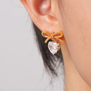 Detail view of a golden bow stud earring featuring a heart-shaped white zircon.
