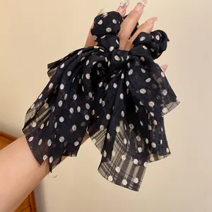 Κοντινό πλάνο ενός κομψού μαύρου scrunchie με φιόγκο και λευκά πουά στο χέρι μιας γυναίκας