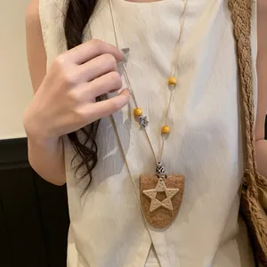 Détail d'un collier bohème avec un pendentif étoile tissé et des perles jaunes.