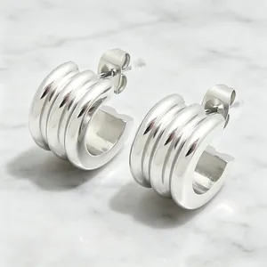 Modern silver stainless steel triple-layer ribbed C-shaped hoop earrings on marble