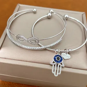 Detailansicht von silbernen Zirkonia-Armreifen mit Hamsa-Hand- und Unendlichkeits-Anhängern