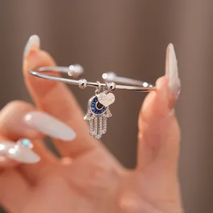Nahaufnahme der Hamsa-Hand und Herzanhänger an einem silbernen Zirkonia-Armreif für Damen
