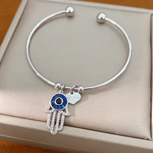 Nahaufnahme von silbernem Armreif mit Hamsa-Hand und blauem Auge-Anhänger