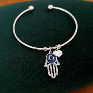 Nahaufnahme eines silbernen Armreifs mit Hamsa-Hand und Herzanhänger auf grünem Samt.