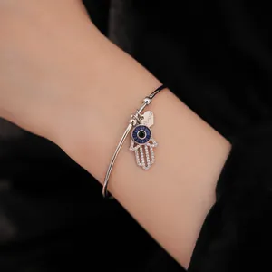 Detailansicht eines silbernen Hamsa-Hand-Armreifs mit blauem bösen Blick am Handgelenk
