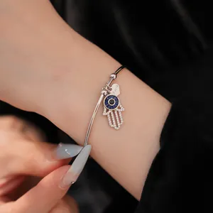 Detailansicht eines silbernen Armreifs mit Hamsa-Hand-Anhänger und blauem Zirkonia-Auge
