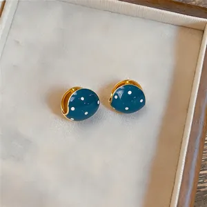 Gedetailleerd overzicht van blauwe emaille oorbellen met witte stippen en goudkleurig metaal