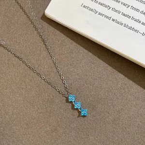 Collier élégant de style français avec trois pendentifs fleurs en zircon bleu sur fond texturé.