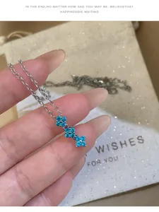 Gros plan d'un collier en argent avec des pendentifs en fleurs de zircon bleu à la main
