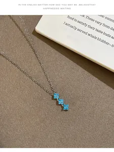 Détail d'un collier en argent avec trois fleurs en zircon bleu posé sur un livre.