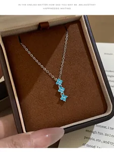 Gros plan d'un collier en argent avec trois pendentifs fleurs en zircon bleu en boîte