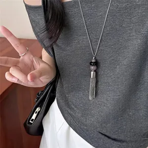 Detailopname van een roestvrijstalen kralenketting met kwastjes gedragen op een grijze top