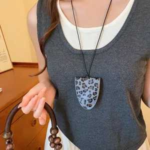 Detail van een brillenhouder ketting met luipaardprint op een grijze trui van een model