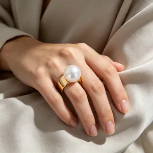 Nahaufnahme eines übergroßen Perlenrings mit breitem goldenem Edelstahlband an der Hand.