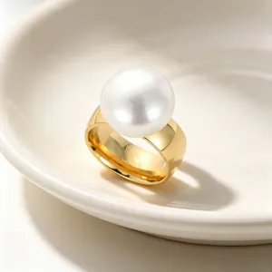 Makroansicht eines breiten Goldrings mit großer weißer Perle auf einem Keramikteller